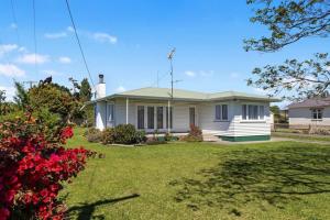 a white house with a yard with red flowers at Retro Cottage in Opotiki CBD in Opotiki