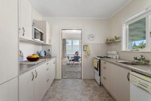 uma cozinha com armários brancos, um lavatório e uma janela em Retro Cottage in Opotiki CBD em Opotiki