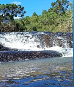 una cascada en un río con árboles en el fondo en Casa de Campo da Vó en Urupema