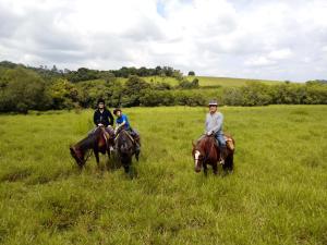 three people riding horses in a grassy field at Pouso do Tropeiro - Cavalgadas Roseta in Baependi