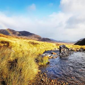 a person is crossing a stream in a field at Baltinna East - by Where Stags Roar in Newtonmore