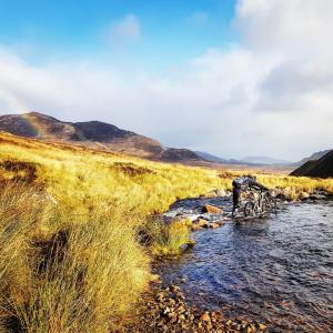 una persona está cruzando un arroyo en un campo en Baltinna East - by Where Stags Roar, en Newtonmore