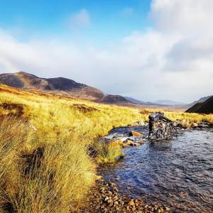 une personne traverse un ruisseau dans un champ dans l'établissement Baltinna East - by Where Stags Roar, à Newtonmore
