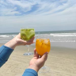 two people holding up two glasses of drinks on the beach at PÉ NA AREIA apartamento térreo in Itapoa