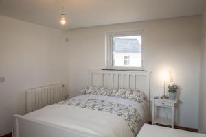 a white bedroom with a bed and a window at Paddy Carrolls Cottage in Ballyconneely