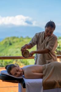 Eine Frau, die auf einem Bett liegt, während ein Mann eine Massage gibt. in der Unterkunft Deep Roots Dive & Yoga Resort in Nusa Penida