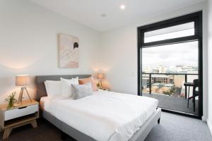 um quarto com uma cama branca e uma grande janela em The East End Apartments by Urban Rest em Adelaide