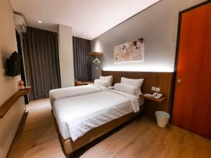 een slaapkamer met een groot bed met witte lakens bij Votel Krakatau Boutique Hotel Semarang in Semarang