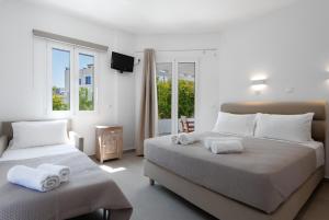 a white bedroom with two beds and a window at KALYPSO ACCOMMODATION SIFNOS in Vathi