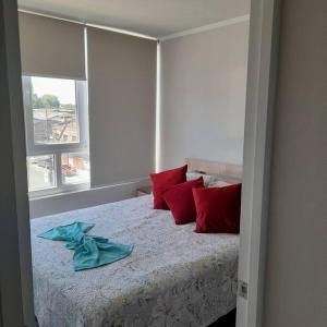 a bedroom with a bed with red pillows and a window at Departamento central en Temuco in Temuco
