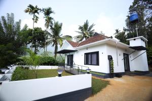 a white house with palm trees in the background at Teaside Inns in Vythiri