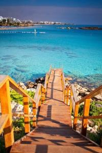 een houten promenade die naar de oceaan leidt op een strand bij Constantinos the Great Beach Hotel in Protaras