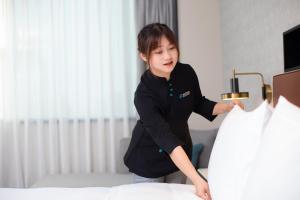 a woman making a bed in a hotel room at Xin'an Yihao Hotel - Near Xiamen Railway Station, near Vientiane City, minibar is free in Xiamen