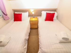 two twin beds in a small room with red pillows at Manderine Lodge in Morpeth