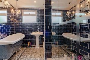 - une salle de bains carrelée de bleu avec deux lavabos et une baignoire dans l'établissement Modern 4 bed home, hottub and traditional pub, à Down Hatherley