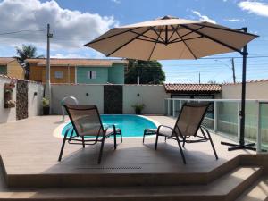 un patio con due sedie e un ombrellone accanto alla piscina di Piscina aquecida, 3 dorms ar condicionado, Cervejeira e Bilhar, a 500 metros do Mar a Bertioga
