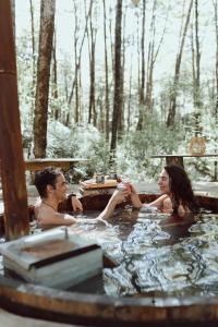 un homme et une femme assis dans un bain à remous dans l'établissement RUKAKUTRAL refugio de bosque, à Pucón