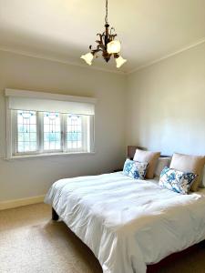 a bedroom with a bed with a chandelier and two windows at Cherry Blossom Cottage - Beechworth-Getaways in Beechworth