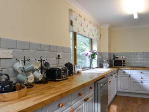 uma cozinha com armários brancos e um balcão de madeira em Rowan House em Glencripesdale