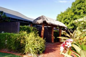 
a woman standing under an umbrella in front of a garden at Mantra Frangipani Broome in Broome
