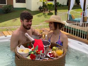 a man and woman sitting in a hot tub with a basket of food at Hotel La Bella Toscana - Exclusive Hotel in Águas de Lindoia