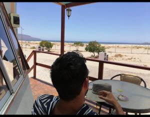 DOMO CAMPING في باهيا انغليسا: رجل يجلس على طاولة ينظر إلى الشاطئ