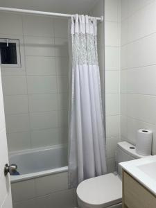 La salle de bains est pourvue d'un rideau de douche blanc et de toilettes. dans l'établissement Hermoso Departamento familiar en condominio, à El Tabo