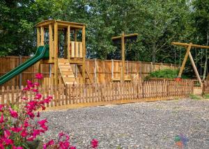 a playground with a wooden fence with a slide at Otters Mead Boutique Lodges in Beetley