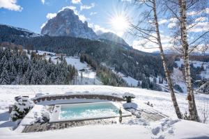 uma banheira de hidromassagem na neve com uma montanha ao fundo em Chalet Villa Carolina em Selva di Val Gardena