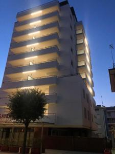 Un alto edificio bianco con un albero davanti di Aparthotel Alessandria a Lignano Sabbiadoro