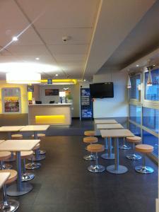 a cafeteria with tables and stools and a tv at ibis Budget Gennevilliers Asnieres in Gennevilliers