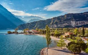 a beach with trees and mountains in the background at Garden Thermae in Nago-Torbole