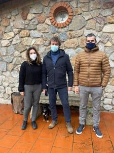 three people wearing masks standing next to a stone wall at La Quercia in Arbus