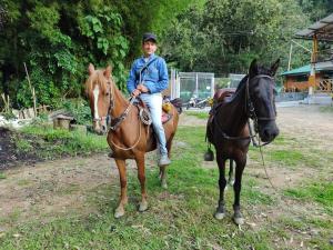 Un joven cabalgando en un caballo junto a otro caballo en Casa Flórez Hotel Campestre en Ibagué