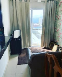 a living room with a couch and a tv and a window at Espaço Mahina - Unidade Dez - Apartamento para temporada Praia Grande Ocian in Praia Grande