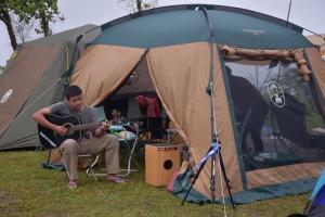 Ein Mann, der vor einem Zelt Gitarre spielt in der Unterkunft ไร่นุชชม รีสอร์ทเขาค้อ in Ban Non Na Yao
