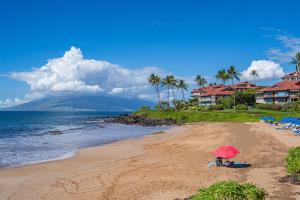 a person sitting on a beach with a red umbrella at Aloha Moon - A Chic and Dreamy Modern Tropical Hideaway! in Wailea