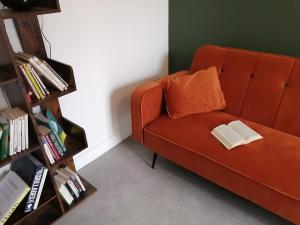 un sofá naranja con una almohada naranja y un libro en Le Gîte du Parc, en La Coquille