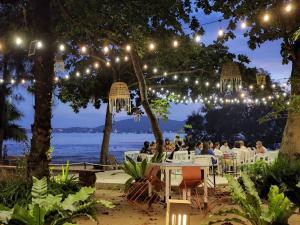 Baan Panwa Resort في شاطئ بنوا: مجموعة من الناس يجلسون على الطاولات تحت الأضواء