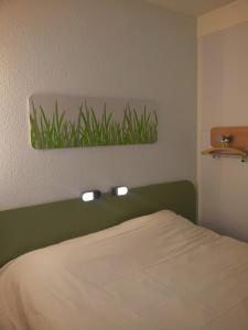 a bedroom with a bed with a green headboard and lights at ibis Budget Gennevilliers Asnieres in Gennevilliers