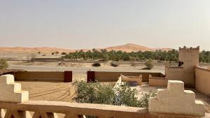 Blick auf die Wüste mit einigen Gebäuden und Bäumen in der Unterkunft Auberge L'oasis in Merzouga