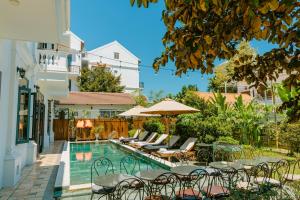 uma piscina com cadeiras e mesas ao lado de um edifício em The Sunshine Hoi An Villa em Hoi An