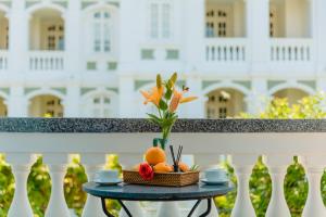 uma mesa com um vaso de flores e frutas numa varanda em The Sunshine Hoi An Villa em Hoi An