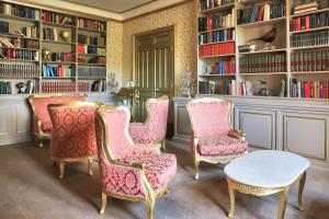 uma biblioteca com cadeiras cor-de-rosa, uma mesa e estantes em Château de Béguin em Lurcy-Lévis