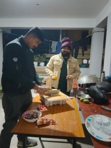 deux hommes debout dans une cuisine préparant de la nourriture sur une table dans l'établissement REMA HOMESTAY, à Itānagar