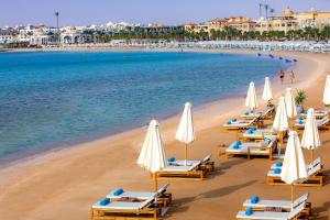 a beach with lounge chairs and white umbrellas at Zen Resort Sahl Hasheesh by TBH Hotels in Hurghada