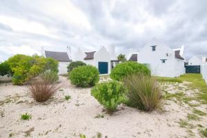 una casa blanca con algunas plantas en la arena en Zuidste Huisie Fisherman's Cottage, en Struisbaai