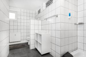 Baño de azulejos blancos con lavabo y aseo en Pension Genat, en Wedemark