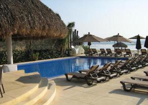 a pool with chairs and umbrellas next to the ocean at Apartamento Acapulco Diamante - Condominium Aura in Acapulco