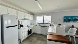 cocina con armarios blancos y nevera blanca en A Minutes Walk To The Beach!, en Caloundra